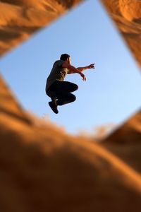 Reflection of man jumping in mirror against sky