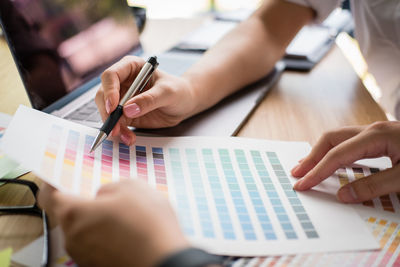 Cropped hands of colleagues deciding colors over paper at desk in office