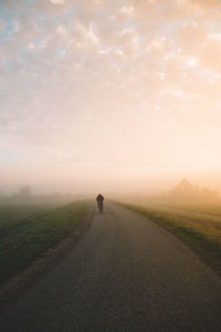 Rear view of man cycling on road during foggy weather against sky
