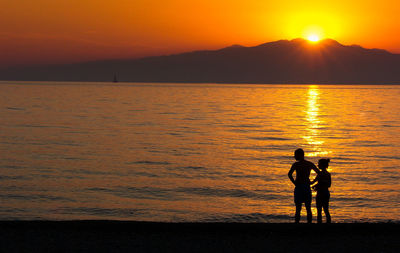 Silhouette couple standing on shore at beach during sunset