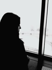 Rear view of silhouette woman looking through window