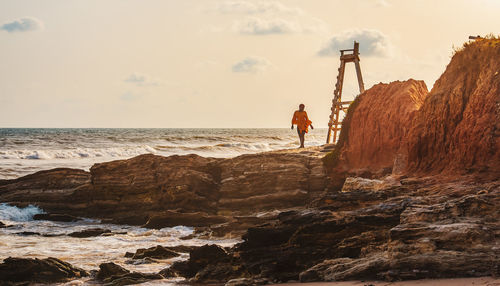 Man on rock at beach against sky