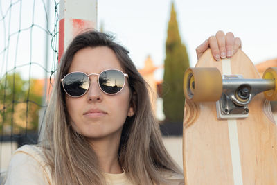 Portrait of beautiful girl seated with a pink skate and the reflection of the sunset on sunglasses