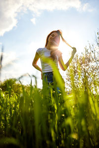 Rear view of woman with arms outstretched standing on field against sky