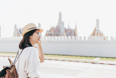 Tourist woman in white shirt and straw hat with brown backpack at wat phra kaew bangkok thailand