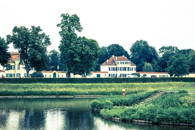 Houses by lake and buildings against clear sky