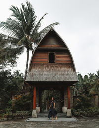 Woman walking on palm tree by building against sky