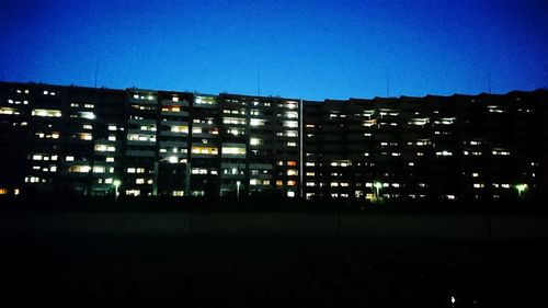 Illuminated city against clear blue sky at night