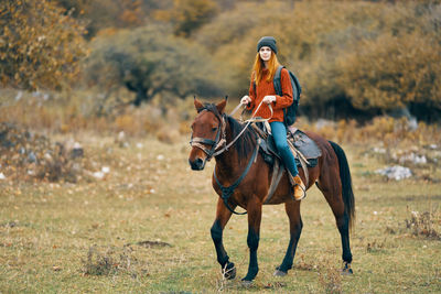 Full length of young woman riding horse on field