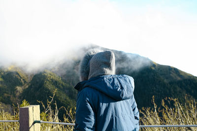 Rear view of woman standing by railing and plants during winter