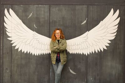 Portrait of woman standing by wall with wings