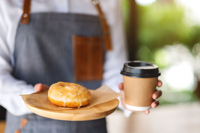 A waitress holding and serving a piece of homemade donut in wooden tray and a paper cup of coffee