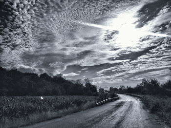 Road passing through landscape against cloudy sky