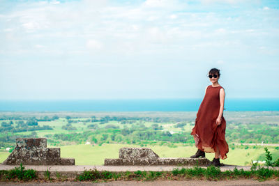 Portrait of young woman wearing sunglasses standing on observation point against cloudy sky