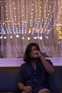 Young man drinking red wine at home with with colorful lights in the ceiling.