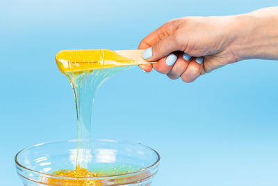 Close-up of hand holding drink against blue background