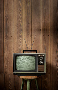 Old television set on stool against wooden wall