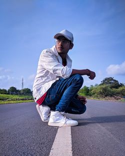 Young man crouching on road against sky