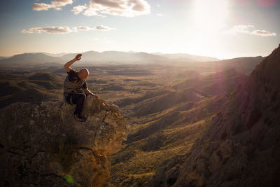 Hiker sitting on rock by mountains against sky