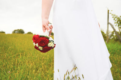 Close-up of hand holding red rose on field