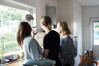 Woman taking selfie while standing with family in kitchen at new home