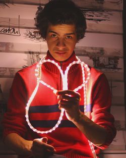Portrait of young man making heart shape with illuminated strip light