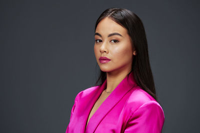 Portrait of young woman standing against gray background