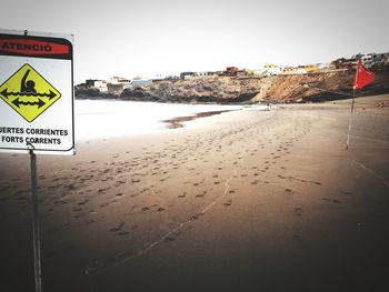 Information sign on beach against clear sky