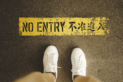 Low section of person standing on no entry sign on road