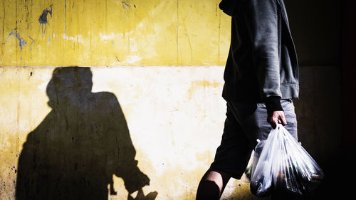 Midsection of man carrying plastic bags while walking by wall