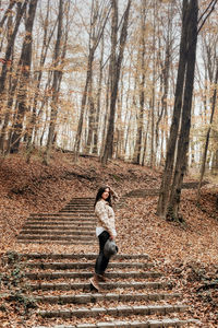 Full length portrait of young woman on stone stairs in forest, autumn, fall.