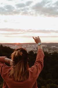 Rear view of woman photographing against sky during sunset