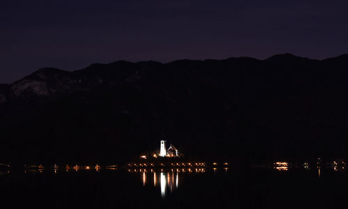 Illuminated city by sea against sky at night