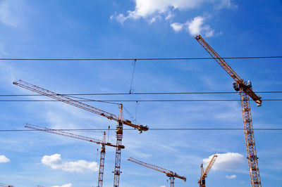 Low angle view of cranes against blue sky