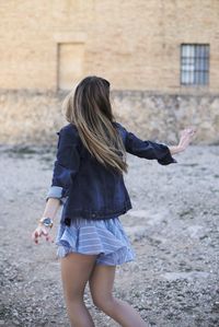 Back view of anonymous young female in trendy outfit turning around with outstretched arms while enjoying freedom in summer