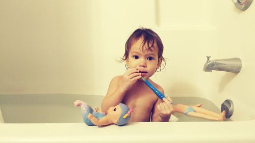 Portrait of cute baby girl holding toothbrush while sitting in bathtub