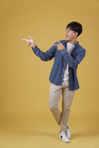 Young man looking away while standing against yellow background