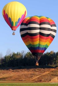 Multi colored hot air balloon flying over trees on field against sky