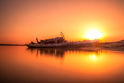 Silhouette cranes by sea against orange sky