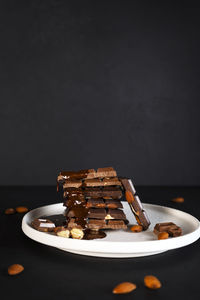 Melted liquid chocolate pours on a plate with pieces of chocolate bars with almond.