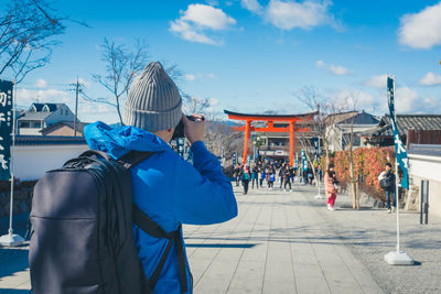 Rear view of photographer photographing people and torii gate while standing on footpath