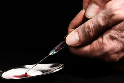 Cropped hand injecting chemical on spoon against black background