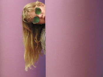 Portrait of girl in sunglasses peeking behind wall