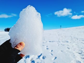 Close-up of person hand on ice against sky