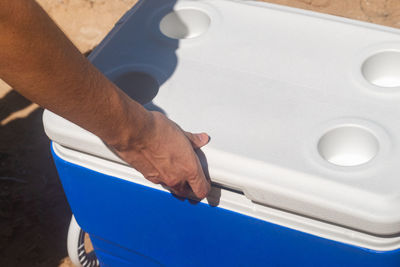 Hand opening a cooler with white top in front of a tropical island beach background from puerto rico