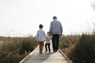 Back view of grandfather and grandchildren strolling hand in hand on boardwalk