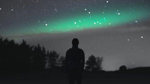 Rear view of silhouette man standing on field against sky at night