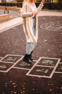 Teenage girl playing hopscotch in park during autumn