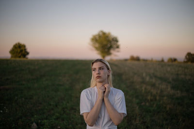 Portrait of young woman standing on field against sky during sunset