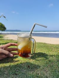 Midsection of woman holding drink at beach against sky